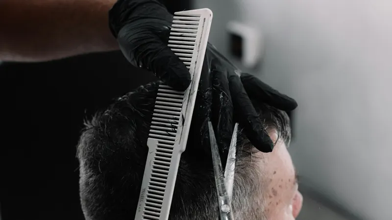 Des mains gantées de noir coupent aux ciseaux, le peigne levé