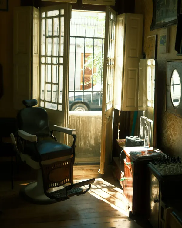 Un fauteuil de barbier ancien dans la lumière d’une porte-fenêtre ouverte sur la rue
